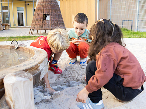 Eine Gruppe Kinder spielt mit Wasser und Sand auf dem Spielplatz