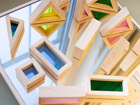 In unserem Bau-Raum gibt es eine Spiegelplatte mit Holzformen, mit bunten transparenten Fenstern