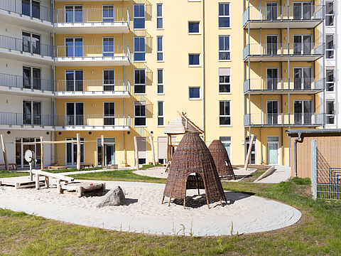 Der Außenbereich ist eine große Rasenfläche mit einem Sandspielplatz und ein paar Spielzelten aus Holz.