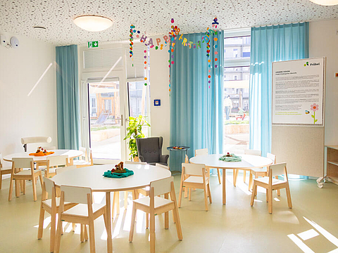 Unser Kinderrestaurant ist ein heller Raum mit runden Tischen, großen Fenstern und hellblauen Vorhängen