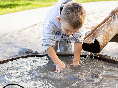 Ein Kind erforscht Matsch auf dem Wasserspielplatz
